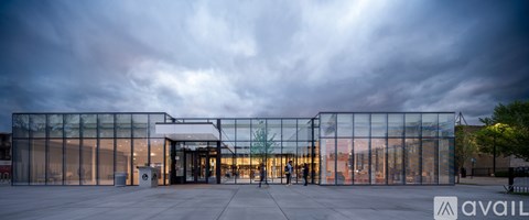 A modern building with a glass facade and a cloudy sky in the background.