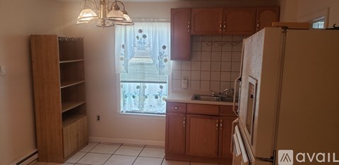 A kitchen with a refrigerator, wooden shelves, and a window with a view of a building.