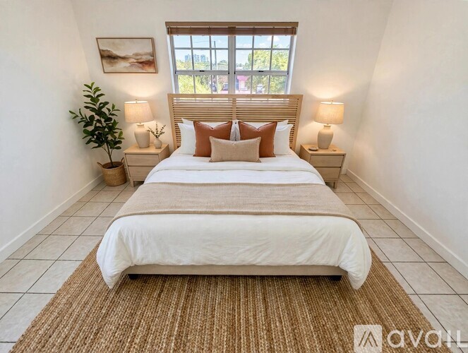 A bedroom with a large bed, two lamps, and a plant.