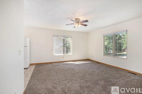 A room with a ceiling fan and two windows.