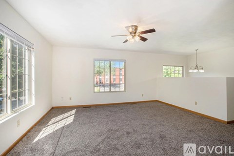 A spacious room with a ceiling fan and two windows.