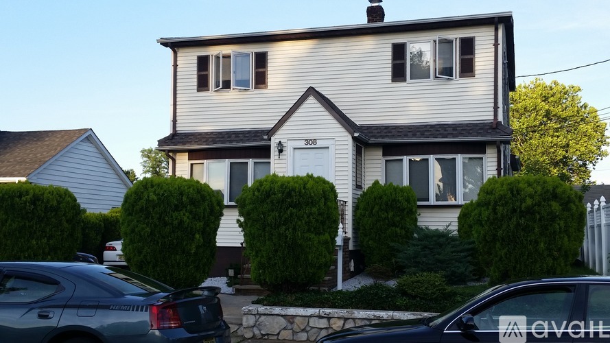 A house with a white door and windows is surrounded by green bushes.