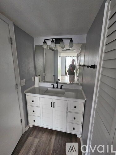 A man is standing in a bathroom with a sink and mirror.