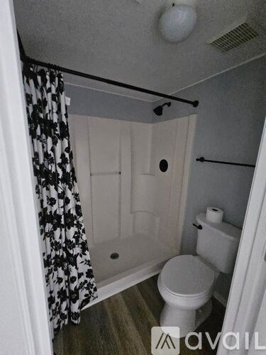 A small bathroom with a toilet, a shower with a black and white curtain, and a white door.