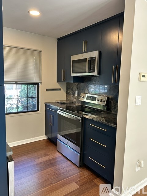 A kitchen with dark blue cabinets and a stainless steel oven and microwave.