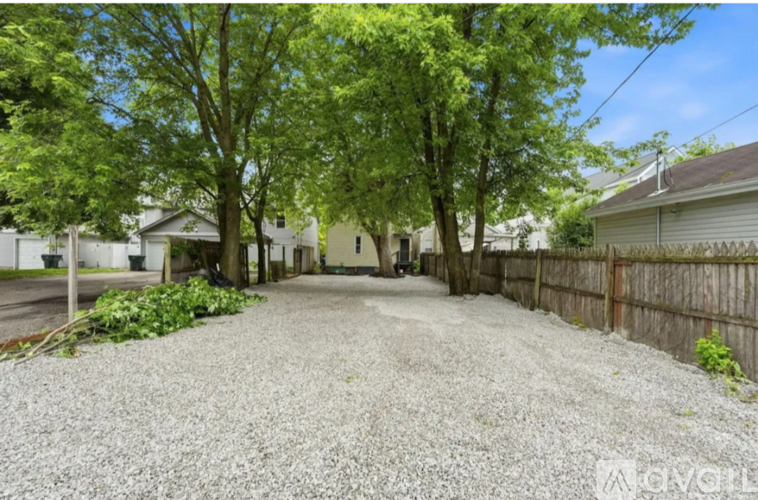 A gravel driveway leads to a house with a wooden fence and green trees.