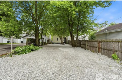 A gravel driveway leads to a house with a wooden fence and green trees.