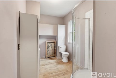 A bathroom with a toilet, a shower, and a wooden floor.