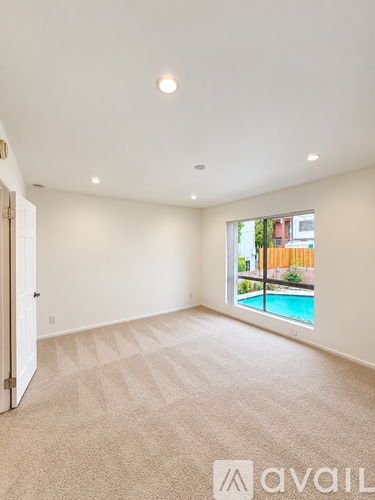A large empty room with a carpeted floor and a window overlooking a pool.