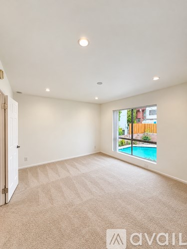 A large empty room with a carpeted floor and a window overlooking a pool.