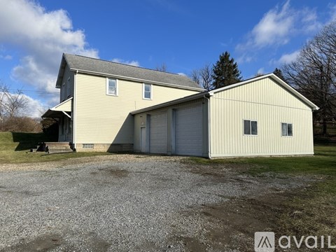 A large, two-story building with a garage door is situated in a gravel lot.
