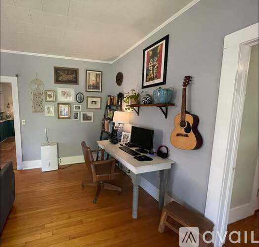 A room with a desk, chair, and a guitar hanging on the wall.