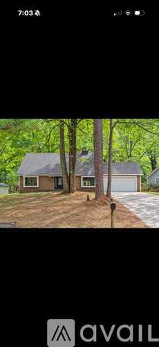 A house with a brown roof and a white garage door is surrounded by trees.