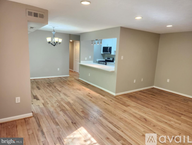 A spacious room with wooden flooring and a kitchenette in the background.