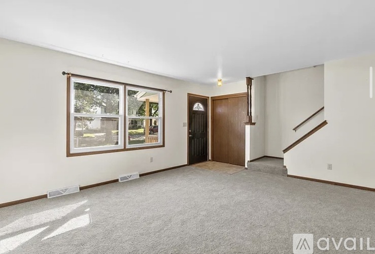 A room with a carpeted floor, a door, and a staircase.