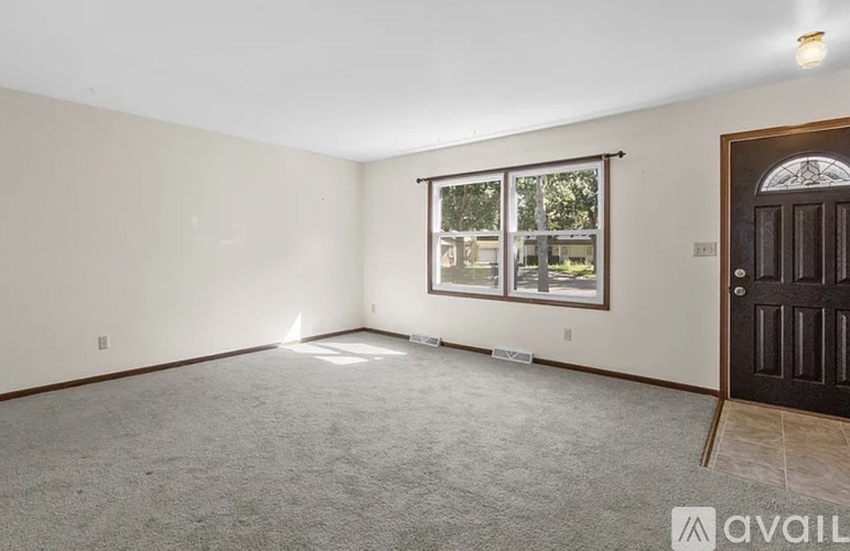 A room with a carpeted floor, a door, and a window with a view of a building outside.