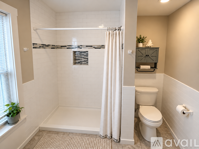 A bathroom with a toilet, a shower with a white curtain, and a window with a plant on the sill.