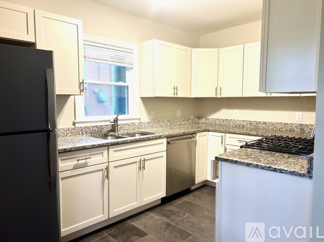A kitchen with black fridge, white cabinets and granite countertops.