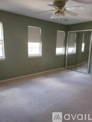 A room with a ceiling fan and three windows.