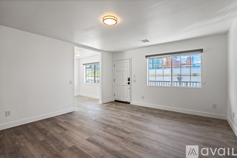 A spacious room with wooden flooring and a large window with a view of a cityscape.