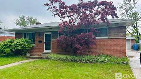 A house with a red brick exterior and a tree with purple leaves in front.