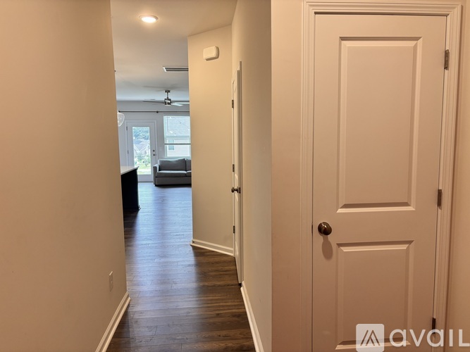 A hallway with a white door and a black couch in the background.