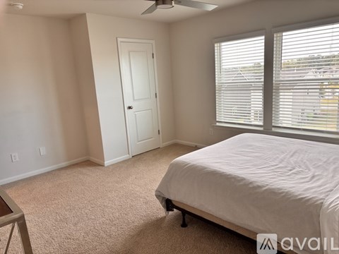 A bedroom with a bed, carpet, and a window with blinds.