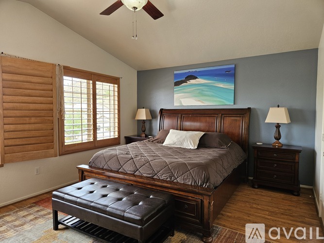 A bedroom with a large bed, a ceiling fan, and a painting of a beach scene on the wall.