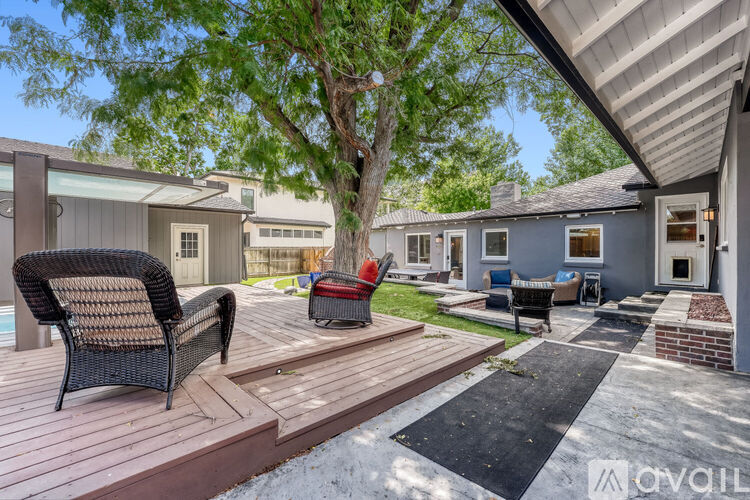 A patio with a black wicker chair and a red chair is surrounded by a wooden deck.
