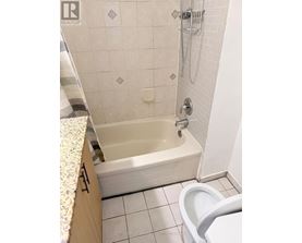 A white tiled bathroom with a bathtub and toilet.