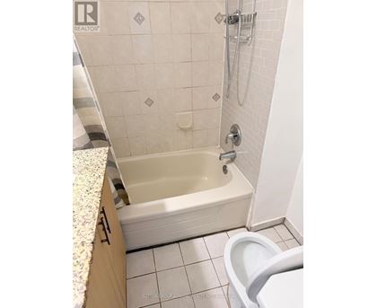 A white tiled bathroom with a bathtub and toilet.