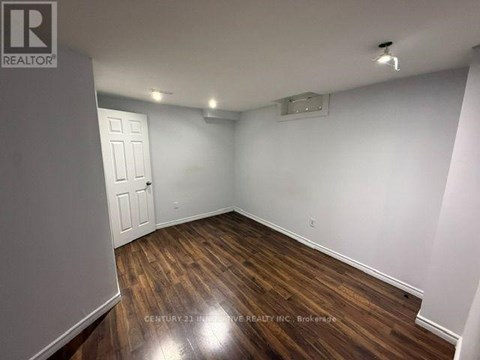 A room with wooden floors and white walls, with a door on the left and a light on the ceiling.