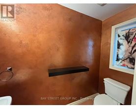 A bathroom with a toilet, a shelf and a painting on the wall.