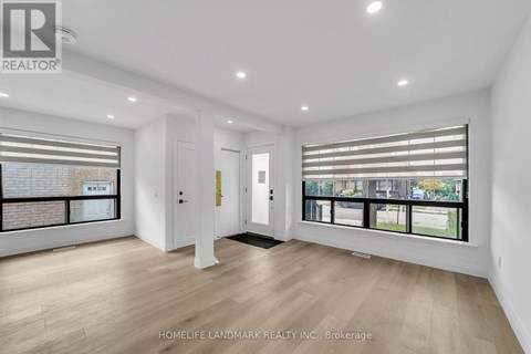 A spacious room with wooden flooring and large windows.