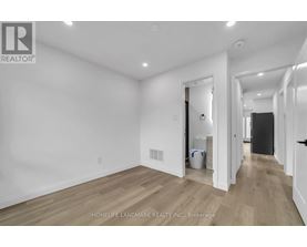 A white room with wooden flooring and a doorway leading to another room.