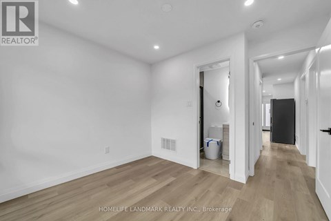 A white room with wooden flooring and a doorway leading to another room.