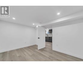 A white room with wooden flooring and a doorway leading to another room.