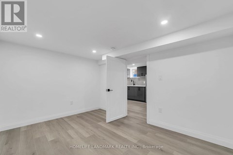 A white room with wooden flooring and a doorway leading to another room.