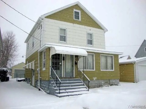 A yellow house with a white roof and a snow-covered front yard.