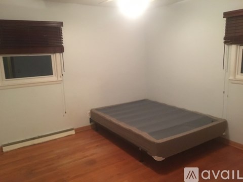 A bed in a room with wooden floors and a window with blinds.