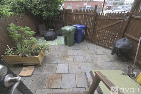 A backyard with a wooden fence and a green trash can.