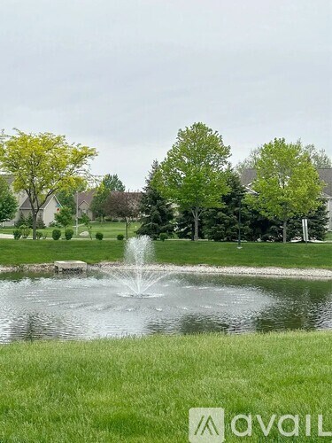 A fountain in the middle of a pond surrounded by green grass and trees.