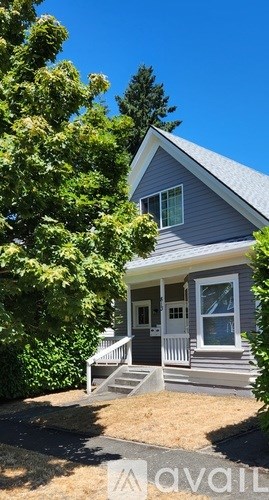 A house with a grey roof and white trim is surrounded by greenery.