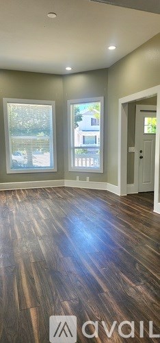 A room with wooden flooring and a window showing a house outside.