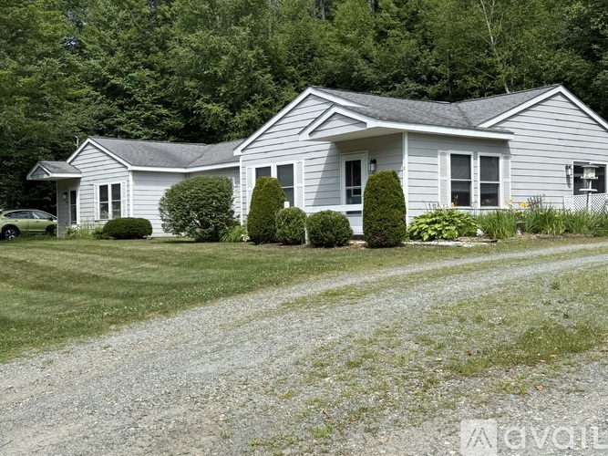 A house with a grey roof and white walls is surrounded by greenery.