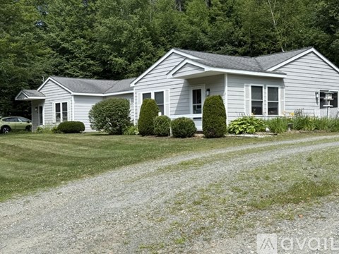 A house with a grey roof and white walls is surrounded by greenery.