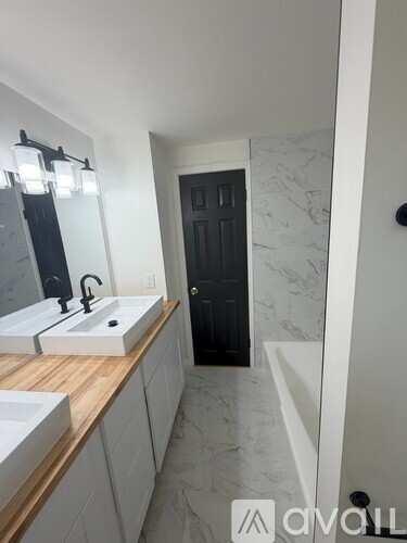 A bathroom with a sink, mirror, and a black door.