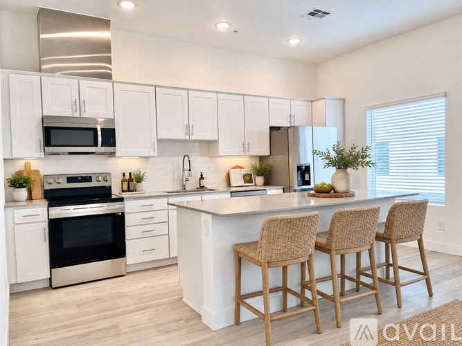 A kitchen with white cabinets and a large island with three chairs.