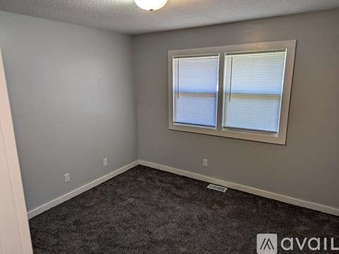 A room with a carpeted floor, a window with blinds, and a light fixture on the ceiling.