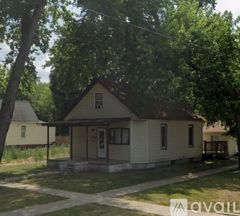 A small house with a porch is surrounded by trees and grass.